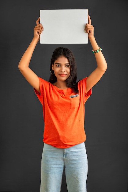 Une jeune fille ou une femme d'affaires tenant une pancarte dans ses mains sur un fond gris