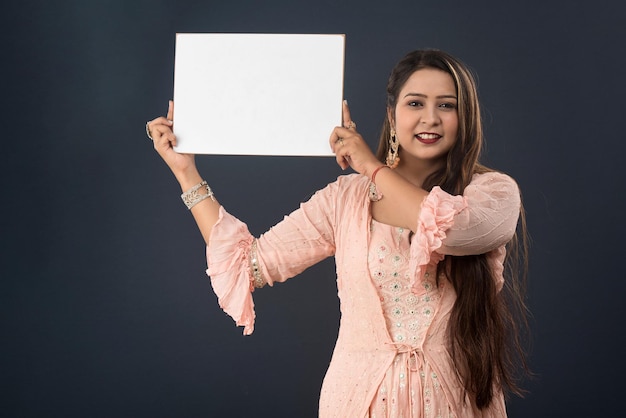 Une jeune fille ou une femme portant une robe traditionnelle indienne tenant une pancarte dans ses mains sur fond gris