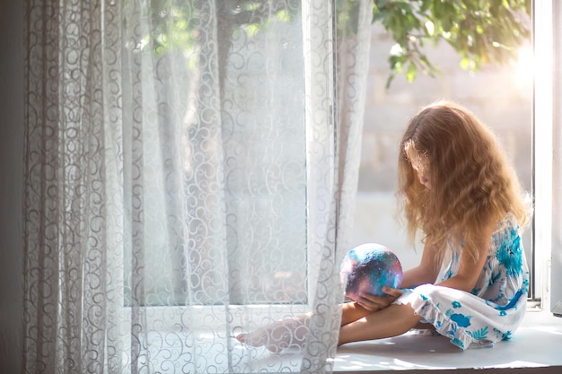 La jeune fille sur la fenêtre de la maison tient une lampe en forme de planète un globe environnement pacifique de l'écologie de la paix