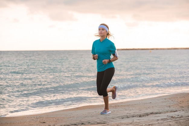 Photo jeune fille fit courir sur la plage au lever du soleil le matin