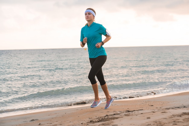 Jeune fille fit courir sur la plage au lever du soleil le matin