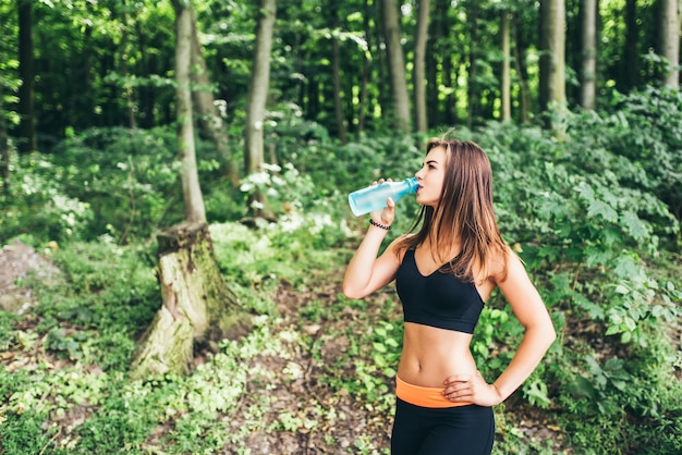 Jeune fille fitness, boire de l&#39;eau dans le parc