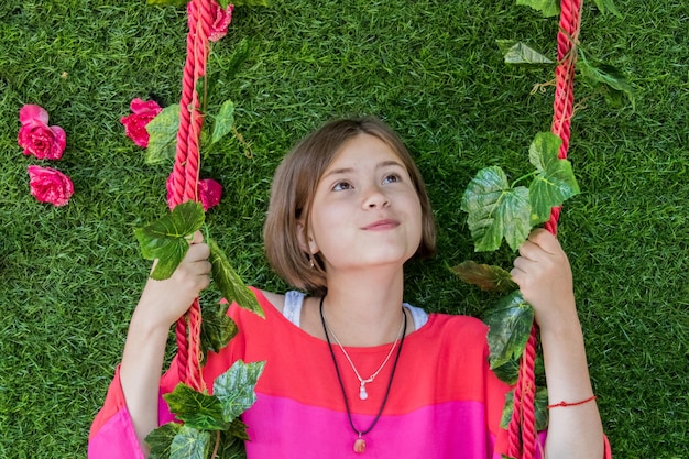 Jeune fille sur fond de bascule sont de l'herbe verte et des fleurs roses