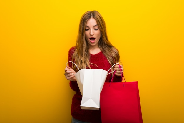 Jeune fille sur fond jaune vibrant surpris en tenant beaucoup de sacs