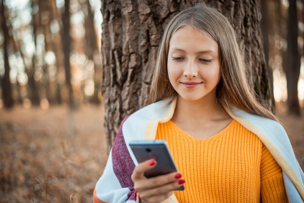 Jeune fille en forêt pleine de feuillage lumineux autour de la navigation sur Internet en communiquant avec des amis