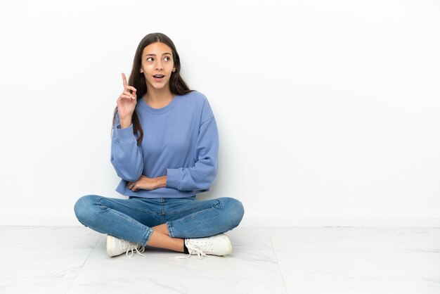 Jeune fille française assise sur le sol en pensant à une idée pointant le doigt vers le haut