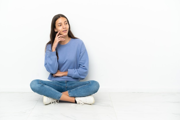 Jeune fille française assise sur le sol pensant à une idée tout en levant les yeux