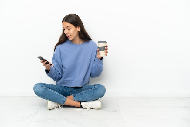 Jeune fille française assise sur le sol tenant du café à emporter et un mobile