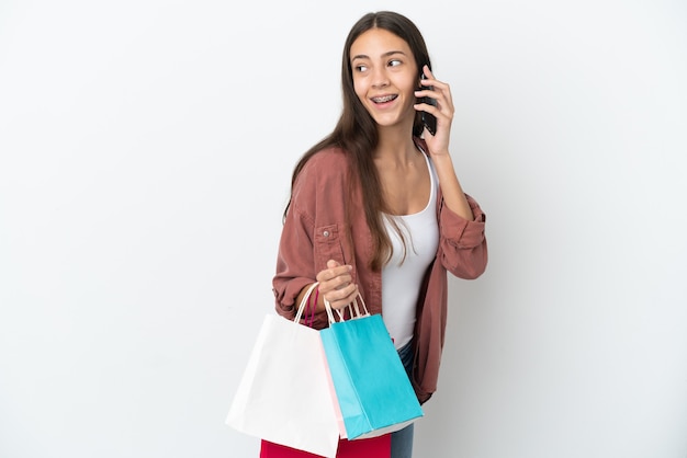 Jeune fille française isolée sur fond blanc tenant des sacs à provisions et appelant un ami avec son téléphone portable