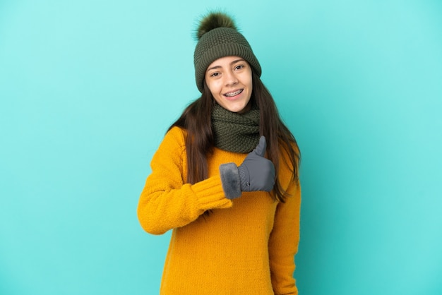 Jeune fille française isolée sur fond bleu avec un chapeau d'hiver donnant un geste de pouce en l'air