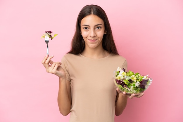 Jeune fille française isolée sur fond rose tenant un bol de salade avec une expression heureuse