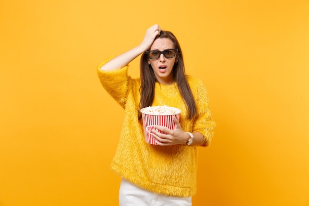 Jeune fille frustrée et inquiète dans des lunettes imax 3d mettant la main sur la tête en regardant un film tenant un seau de pop-corn isolé sur fond jaune vif. Les gens ont des émotions sincères dans le style de vie du cinéma.