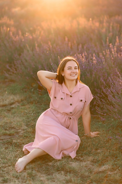 Une jeune fille gaie dans une robe rose et un chapeau de paille dans ses mains se tient parmi les buissons de lavande