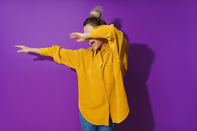 Jeune fille gaie portant une chemise jaune dansant sur fond violet