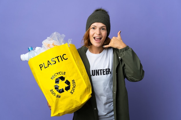 Jeune fille géorgienne tenant un sac plein de bouteilles en plastique à recycler en faisant un geste téléphonique. Rappelle-moi signe