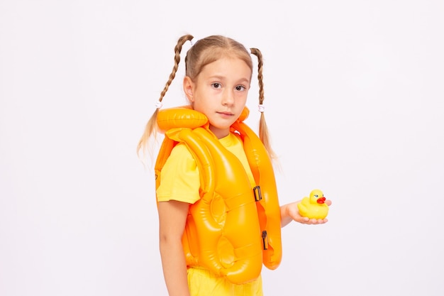 Jeune fille avec gilet de sauvetage jaune et canard en caoutchouc sur fond blanc.