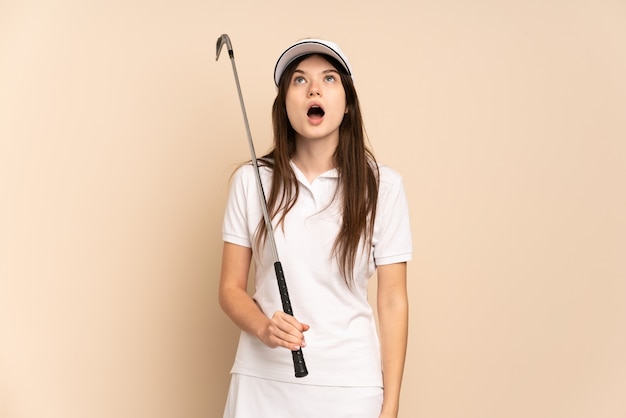 Jeune fille de golfeur isolée sur beige en levant et avec une expression surprise