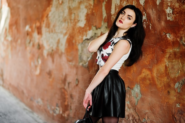 Jeune fille goth sur une jupe en cuir noir avec sac à dos posée contre le mur de grunge.