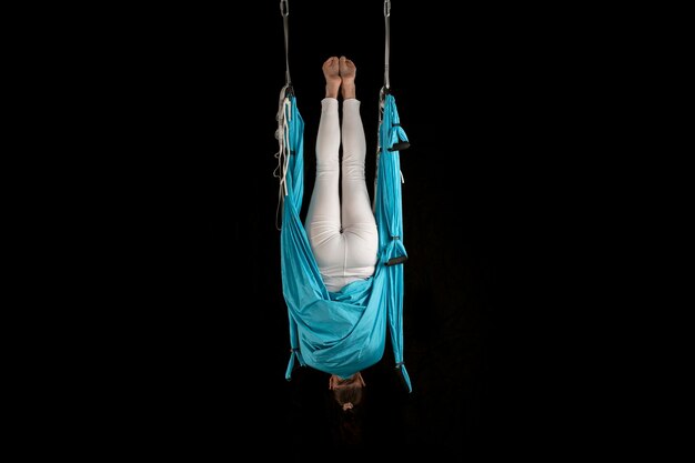 Jeune fille gymnaste en vêtements de sport faisant des étirements tout en étant suspendu à l'envers Aero fly yoga isolé sur fond noir