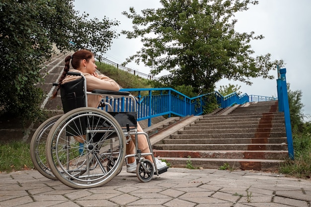 Une jeune fille handicapée est assise dans un fauteuil roulant devant les escaliers. Le concept d'un fauteuil roulant, d'une personne handicapée, d'une vie pleine, d'une personne paralysée, handicapée, des soins de santé, de la solitude.