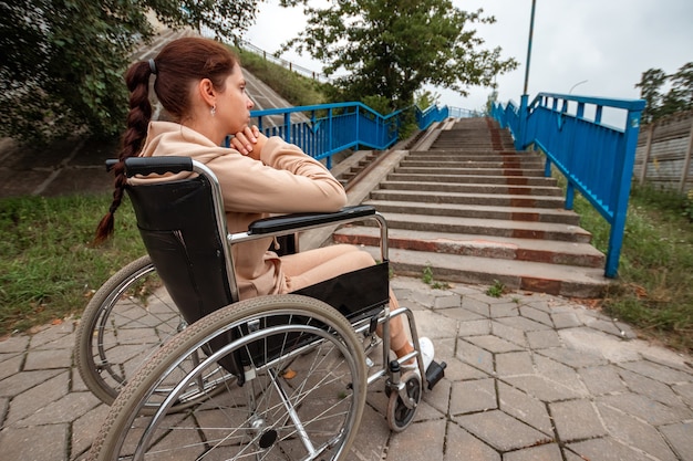 Une jeune fille handicapée est assise dans un fauteuil roulant devant les escaliers. Le concept d'un fauteuil roulant, d'une personne handicapée, d'une vie pleine, d'une personne paralysée, handicapée, des soins de santé, de la solitude.