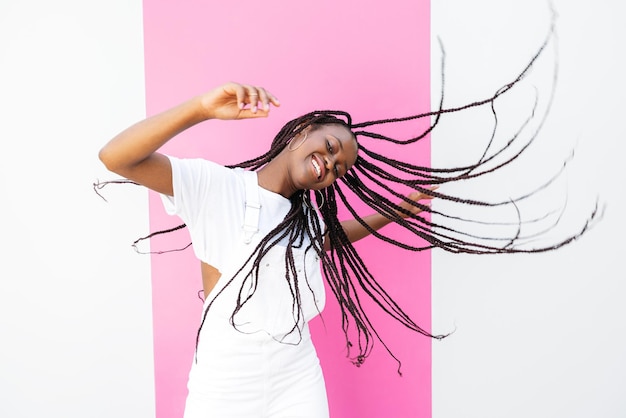 Une jeune fille heureuse aux cheveux tressés qui s'amuse au mur blanc à rayures roses.