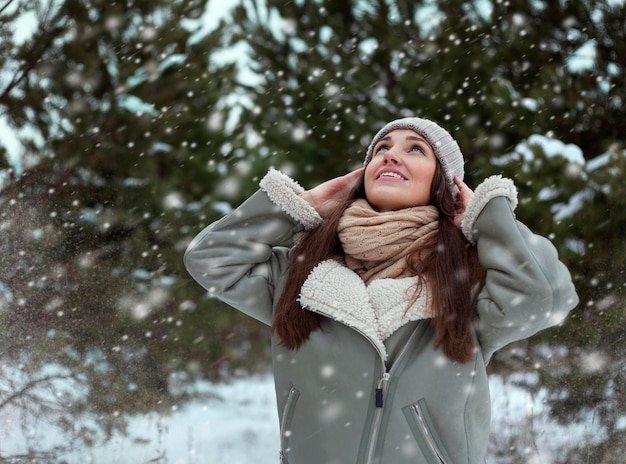 Une jeune fille heureuse dans un parc d'hiver qui regarde la chute de neige