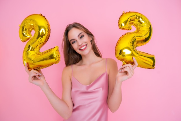 Jeune fille heureuse détient un ballon en feuille d'or isolé sur fond rose concept de fête d'anniversaire