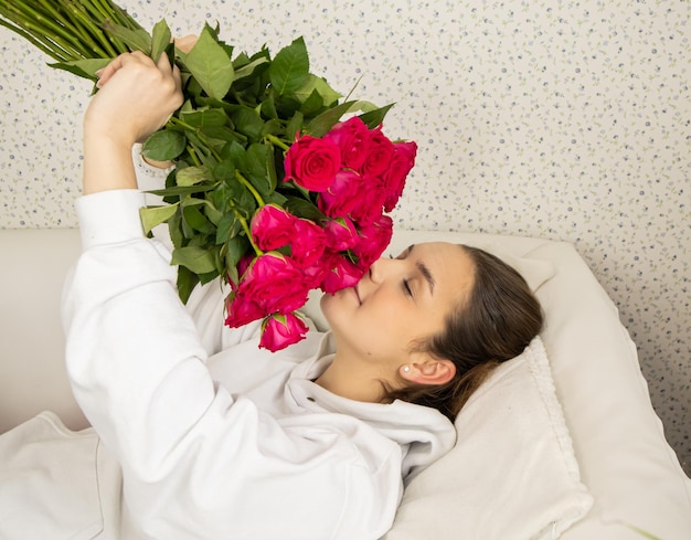 Une jeune fille heureuse est allongée sur le lit et sent les roses les yeux fermés