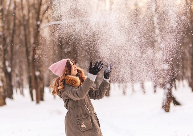 Jeune fille heureuse joue avec la neige dans le parc