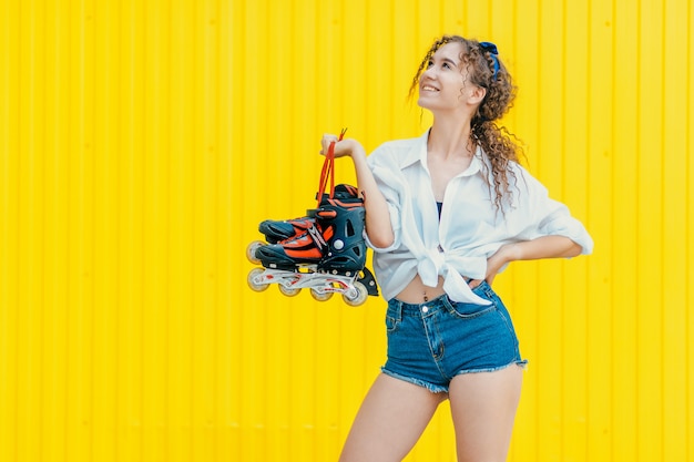 Jeune fille heureuse tenant des rouleaux sur mur jaune