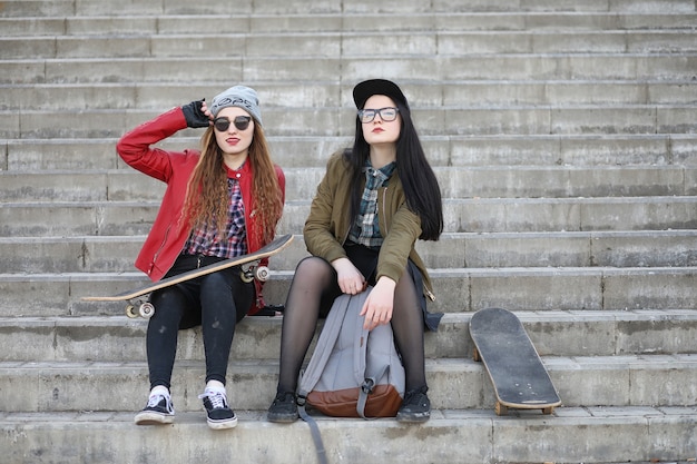 Une jeune fille hipster fait du skateboard. Copines de filles pour une promenade en ville avec une planche à roulettes. Sports de printemps dans la rue avec une planche à roulettes.