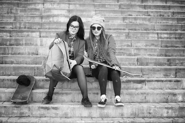 Une jeune fille hipster fait du skateboard. Copines de filles pour une promenade en ville avec une planche à roulettes. Sports de printemps dans la rue avec une planche à roulettes.