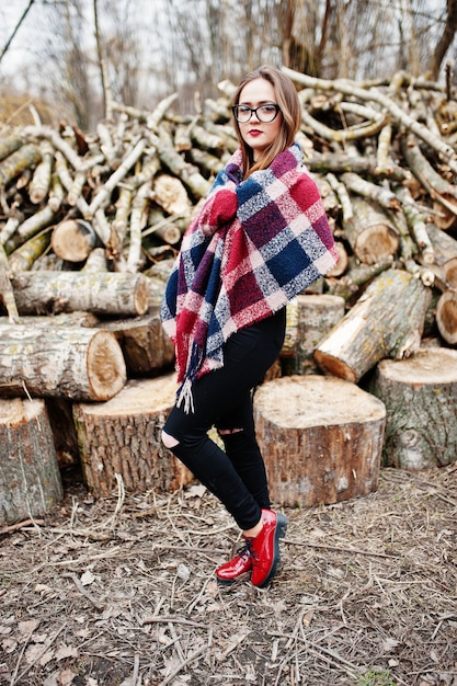 Jeune fille hipster porter sur la couverture et des lunettes contre des souches en bois sur bois.