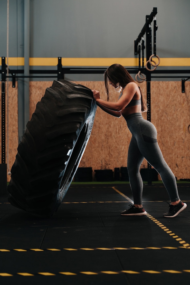 Photo jeune fille hispanique avec des muscles forts soulevant une roue dans un gymnase crossfit
