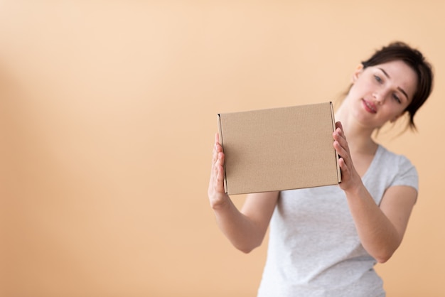 La jeune fille avec intérêt examine la boîte de côté sur un fond beige.