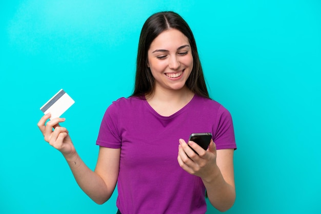 Jeune fille isolée sur fond bleu achetant avec le mobile avec une carte de crédit