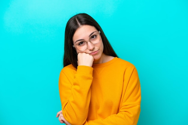 Jeune fille isolée sur fond bleu avec des lunettes et avec une expression triste