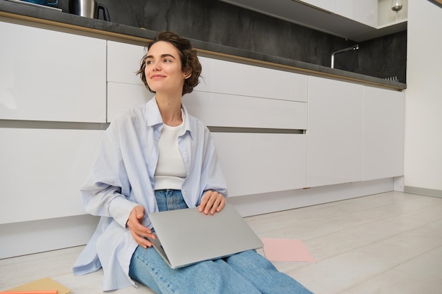 Jeune fille it girl travaille à la pige à la maison est assise sur le sol avec un ordinateur portable fille étudiante fait ses devoirs o