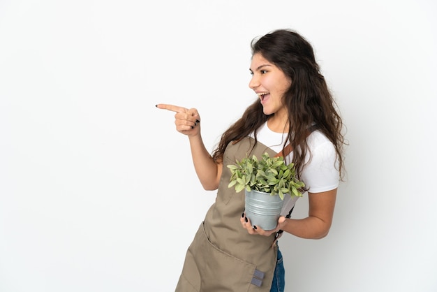 Jeune fille de jardinier russe tenant une plante isolée du doigt sur le côté et présentant un produit