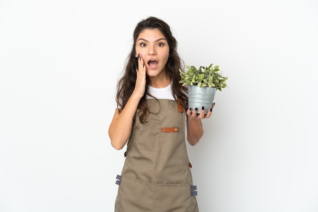 Jeune fille de jardinier russe tenant une plante isolée avec surprise et expression faciale choquée