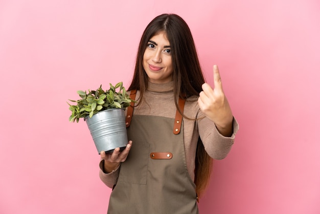 Jeune fille de jardinier tenant une plante isolée sur fond rose faisant le geste à venir