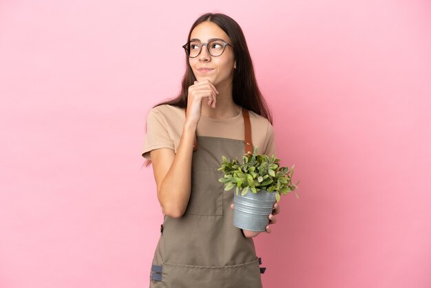 Jeune fille de jardinier tenant une plante isolée sur fond rose et levant