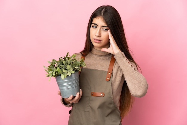 Jeune fille de jardinier tenant une plante isolée sur fond rose avec des maux de tête