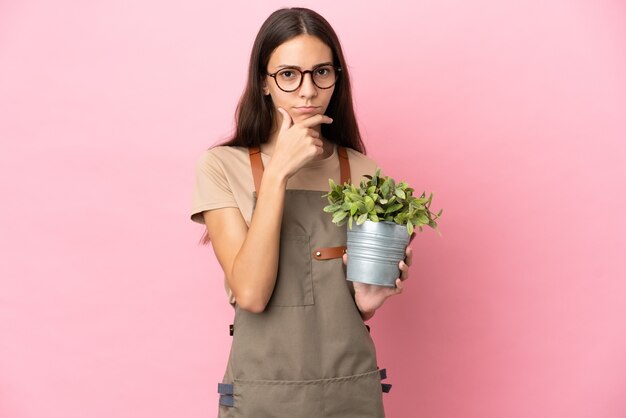 Jeune fille de jardinier tenant une plante isolée sur fond rose pensant