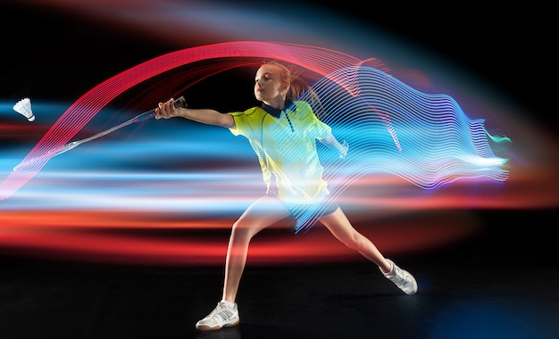 Photo jeune fille jouant au badminton sur le mur sombre du studio