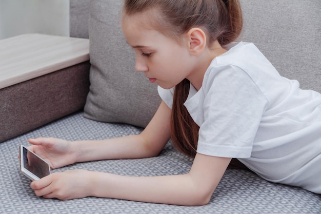 Une jeune fille jouant avec le téléphone en position allongée sur le canapé