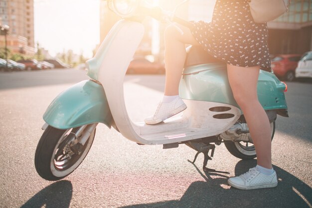 Jeune fille joyeuse au volant de scooter en ville. Portrait d'une femme jeune et élégante avec un cyclomoteur