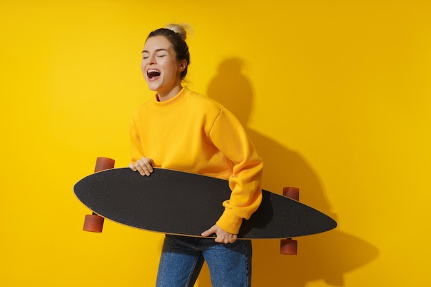 Jeune fille joyeuse avec longboard sur fond jaune