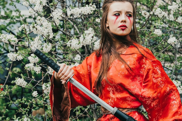 Photo jeune fille en kimano traditionnel dans un jardin fleuri avec katana épée japonaise samouraï à l'image d'une femme guerrière